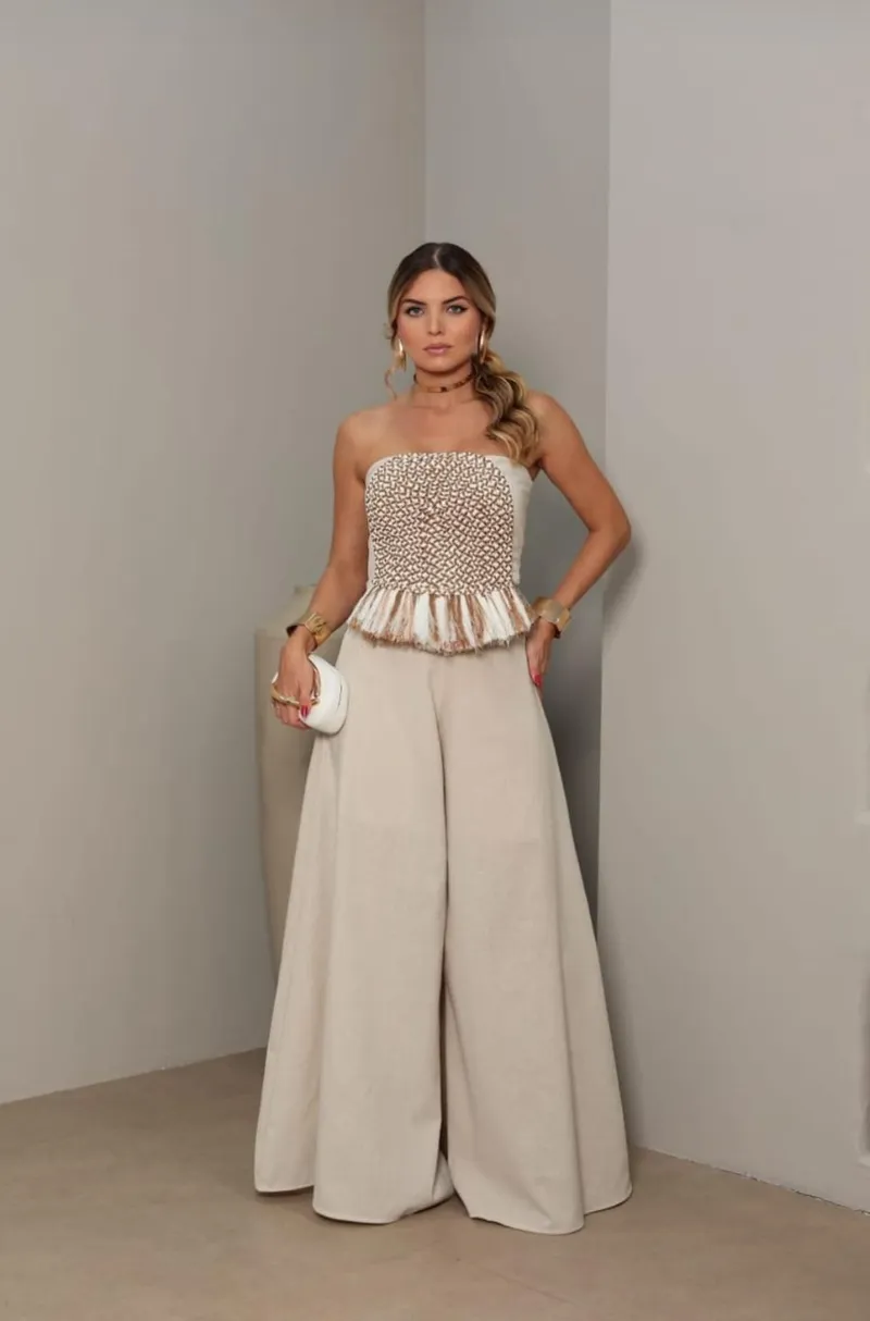 Beige two-piece set: strapless cropped top with textured geometric detailing and fringe trim, with wide-leg palazzo pants.